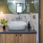 3 BHK Bungalow Green Garden Chembur Mumbai Bathroom Sink Detail With Round Mirror Green Tile Wall Wooden Cabinet And Countertop Basin