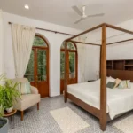 4 BHK Villas Elements Nachinola Goa bedroom with wooden four poster bed arched balcony doors patterned flooring and cream curtains