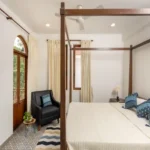 4 BHK Villas Elements Nachinola Goa master bedroom with large wooden windows striped rug white curtains