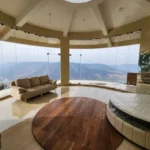 7 BHK Villa Panchgani Mahabaleshwar Interior Curved Glass Lounge Area With Panoramic Valley View Circular Wooden Platform Sofa Seating And Full Height Glass Panels