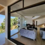 7 BHK Villa Panchgani Mahabaleshwar Interior Living Area Seen Through Large Glass Window Showing Sofa Seating Valley View