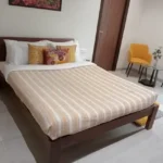 4 BHK Villa Khopoli Bedroom with Striped Bedding and Yellow Chairs