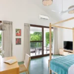 3 BHK Mayberry Villas Anjuna Goa Sunlit Sitting Area With Teal Couch Yellow Armchairs And Pool Facing Windows